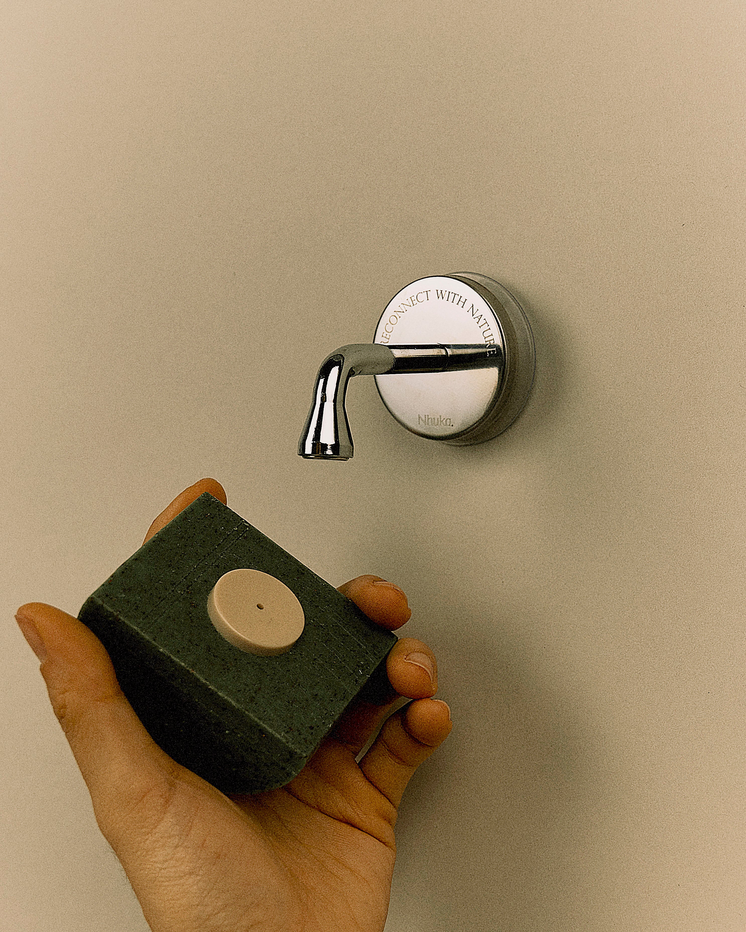 Model demonstrating Nhuka Branch magnetic holder with a Nhuka bar attached via bottle cap insert. Holder keeps bar lifted, dry, and within easy reach. Suction cup attaches securely to glass or tile.