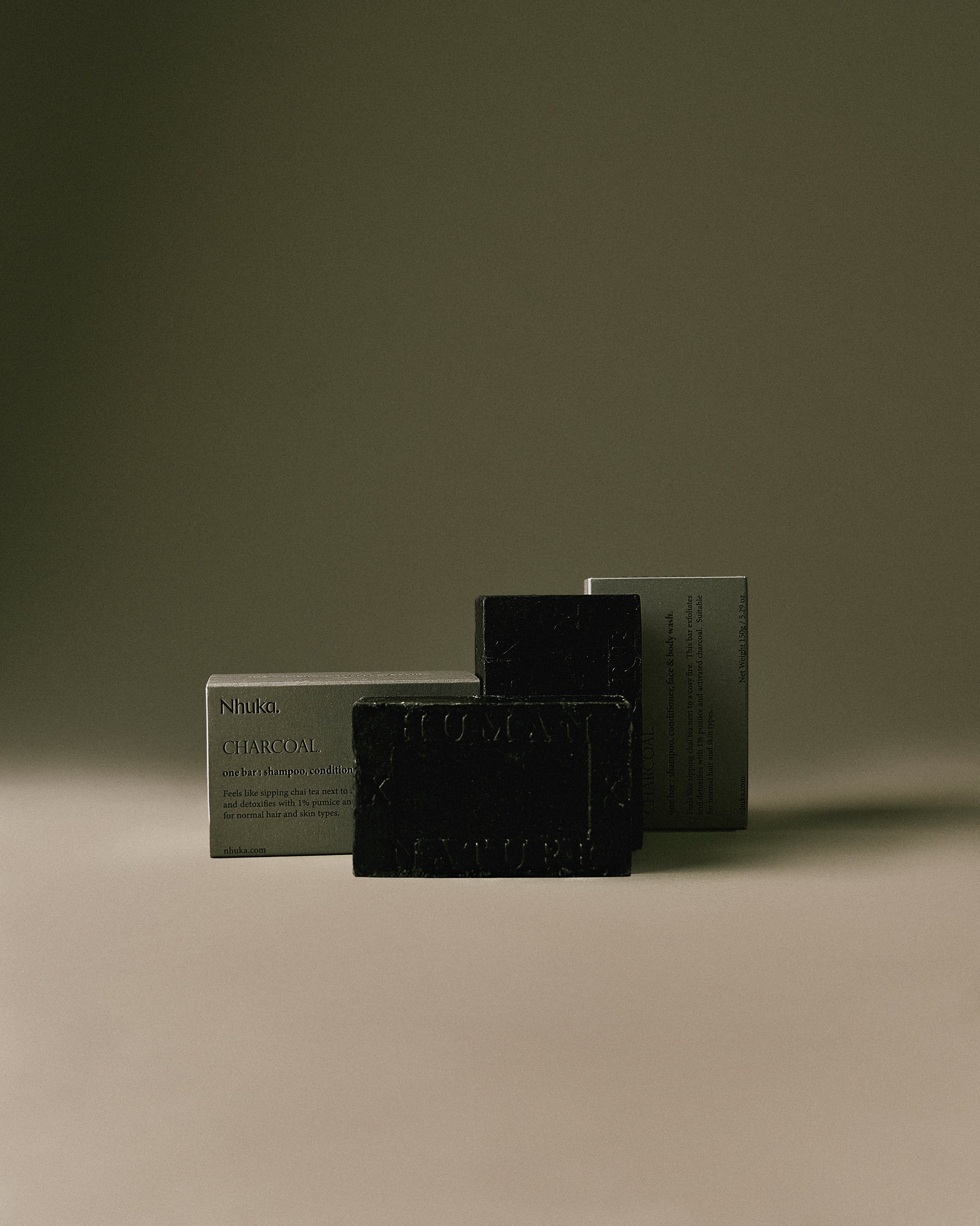 Nhuka Charcoal One Bar packaged in FSC-certified paper. Handmade in Australia, pH-balanced, sulfate-free, silicone-free, and organic. Warming chai scent with cinnamon, ginger, and nutmeg. Exfoliating formula with pumice, designed for hair, face, and body.