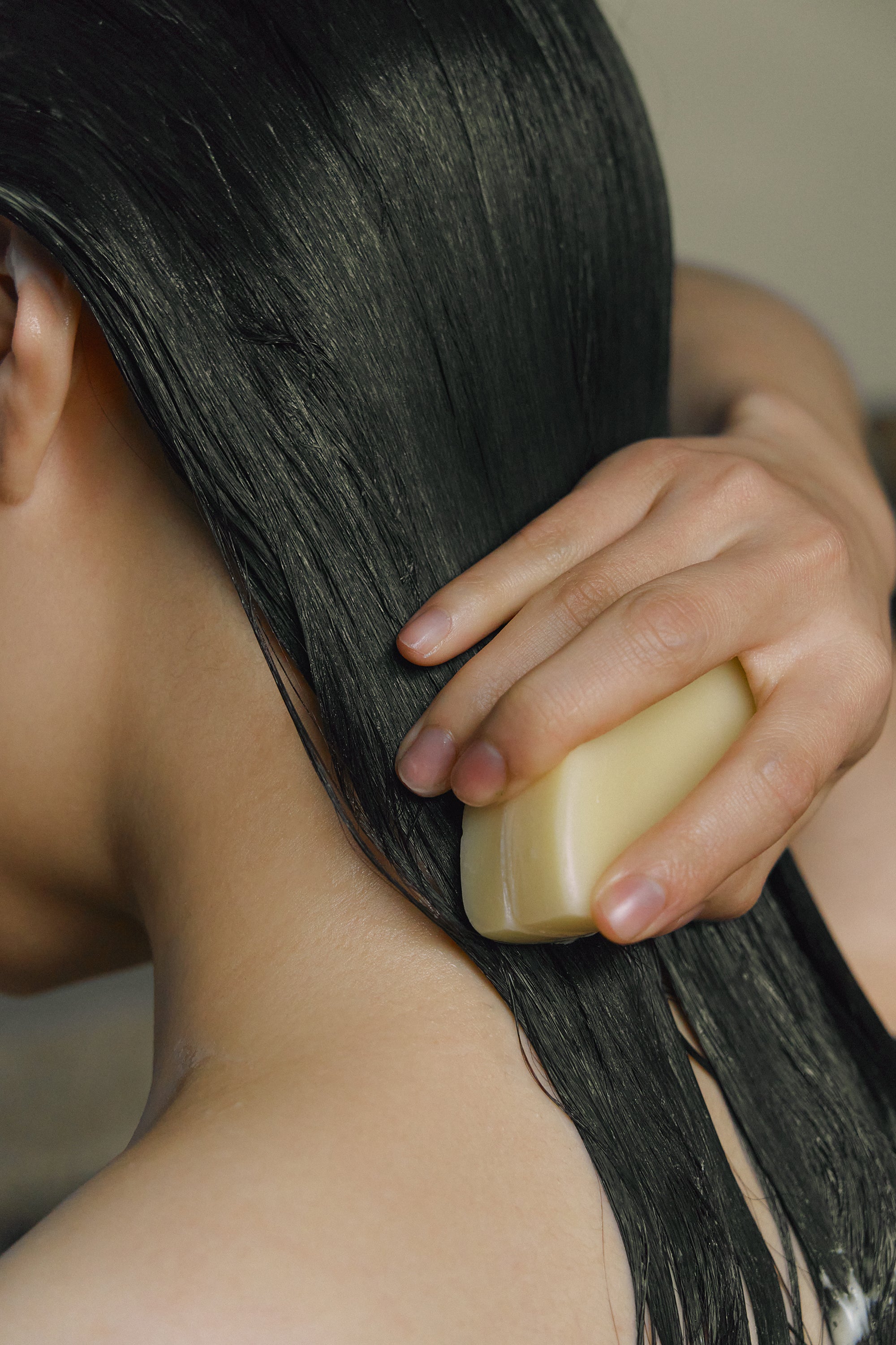 Model applying Nhuka conditioner bar directly onto long wet hair. Silicone-free, pH-balanced, organic formulation designed to nourish and detangle.