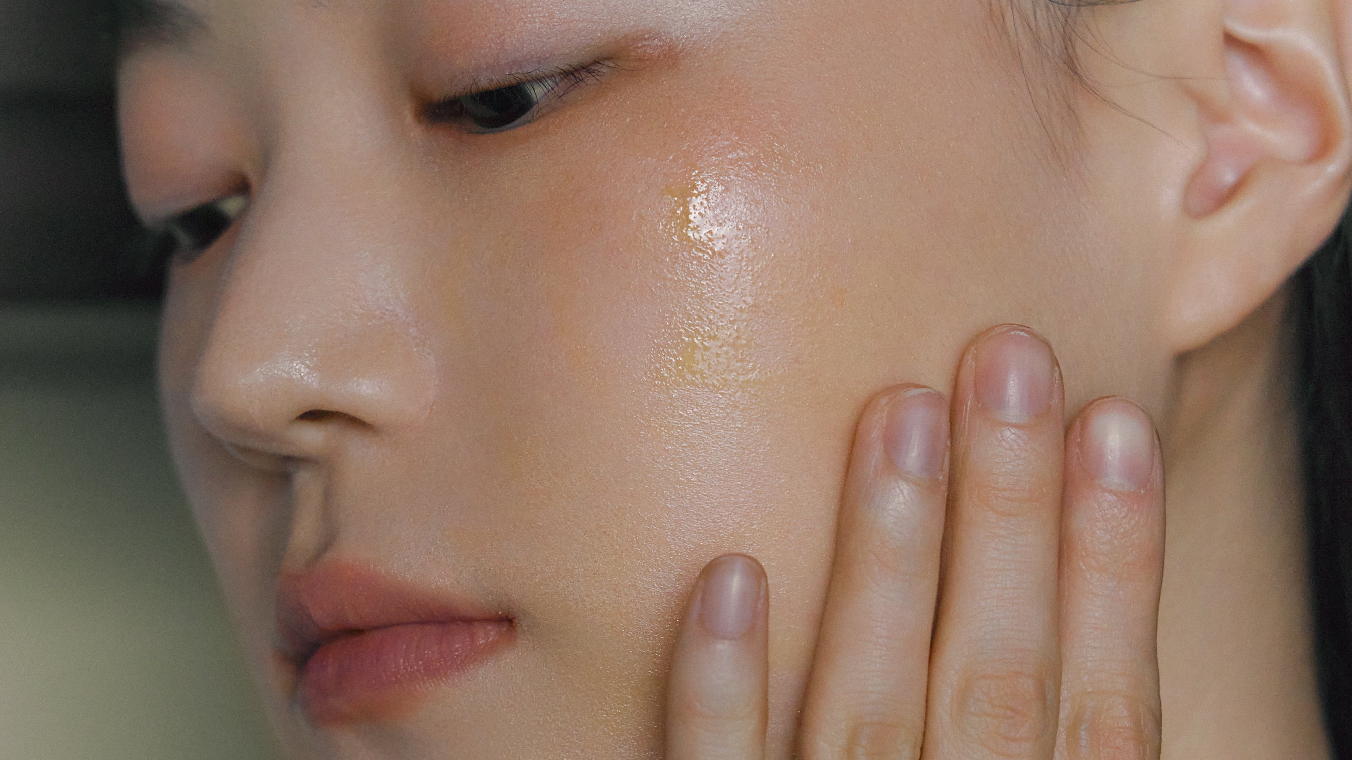 Photo of model using Nhuka face serum on cheek. Deeply restorative with organic plant oils, 5% vitamin c, and 1% bakuchiol oil for dry, mature skin. Handmade in Australia.