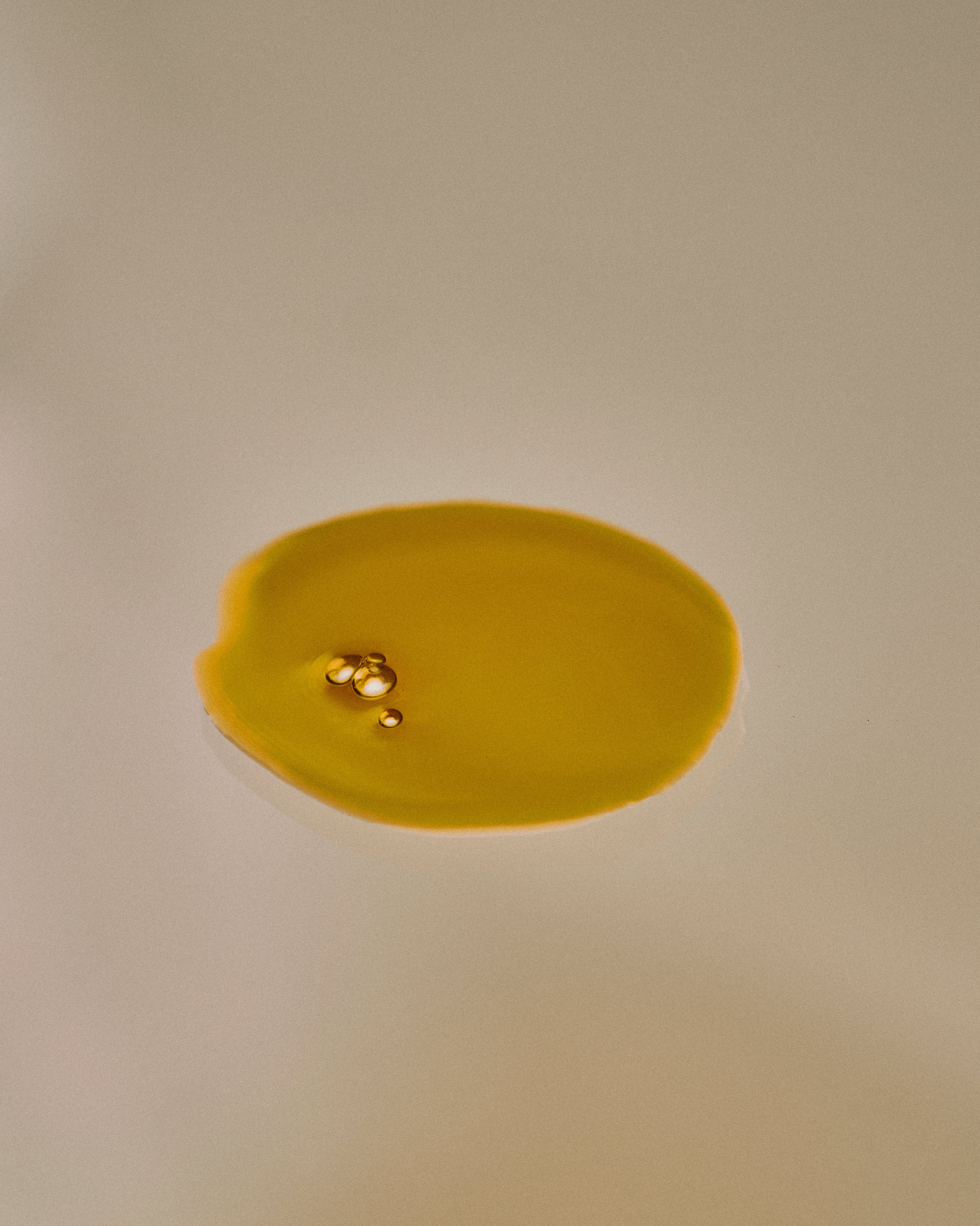 Nhuka Restoration Face Serum texture — golden oil droplets. Formulated with ceramides, hempseed, and rosehip oils to deliver calming hydration for sensitive skin.