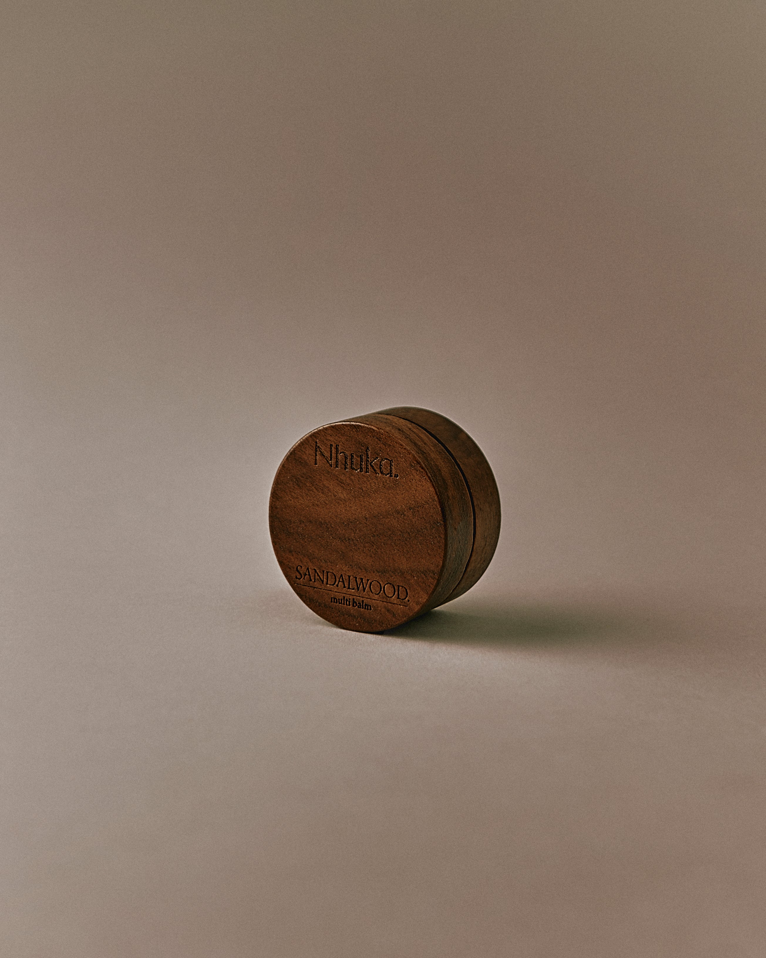 Nhuka Sandalwood Multi Balm shown at an angle. Rich yet silky balm formulated with organic shea butter, hempseed oil, and beeswax to nourish and soothe dry or sensitive skin. Features a warm, earthy scent with hints of sandalwood, sage, and vanilla.