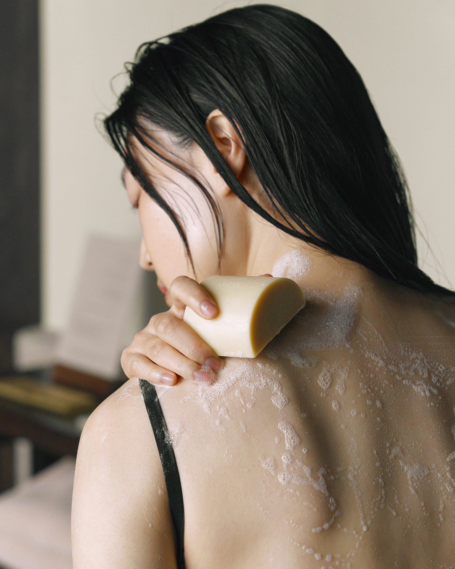Model using Nhuka organic soap on back with visible lather. Gentle, nourishing cleanse for daily skin care.