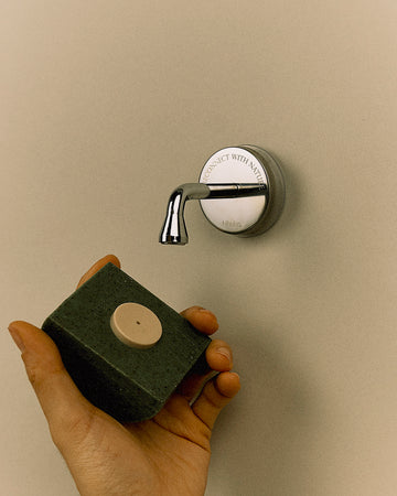 Model demonstrating Nhuka Branch magnetic holder with a Nhuka bar attached via bottle cap insert. Holder keeps bar lifted, dry, and within easy reach. Suction cup attaches securely to glass or tile.