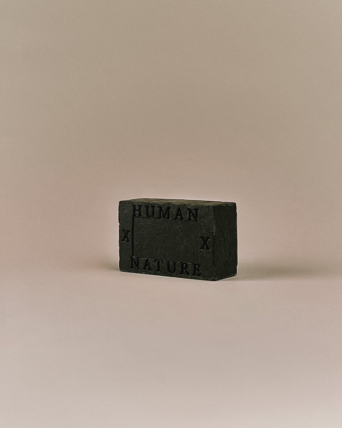 Nhuka Charcoal One Bar shown at an angle with Human x Nature emboss. Handmade in Australia, pH-balanced, sulfate-free, silicone-free, and organic. Warming chai scent with cinnamon, ginger, and nutmeg. Contains pumice for exfoliation. Suitable for hair, face, and body.