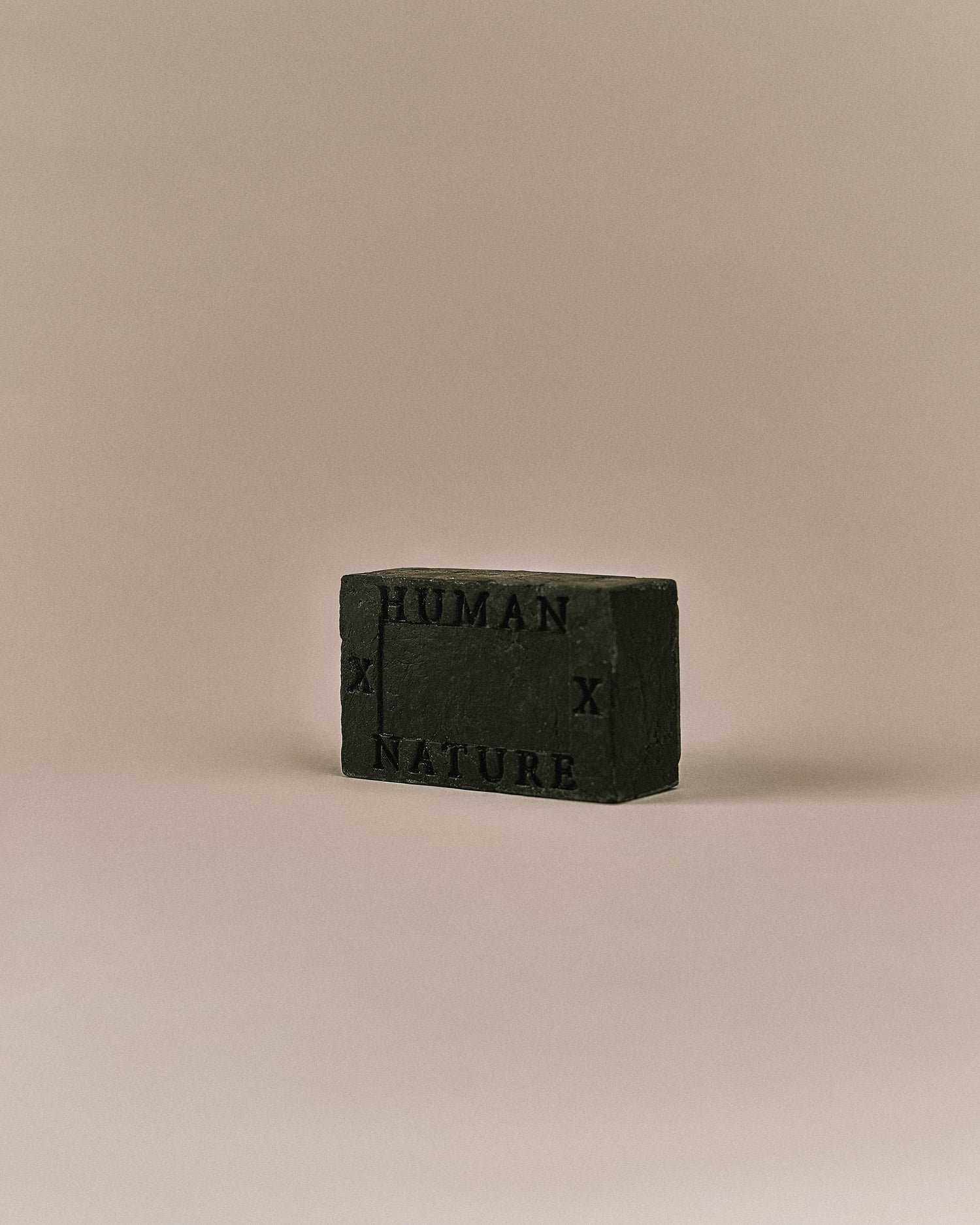 Nhuka Charcoal One Bar shown at an angle with Human x Nature emboss. Handmade in Australia, pH-balanced, sulfate-free, silicone-free, and organic. Warming chai scent with cinnamon, ginger, and nutmeg. Contains pumice for exfoliation. Suitable for hair, face, and body.