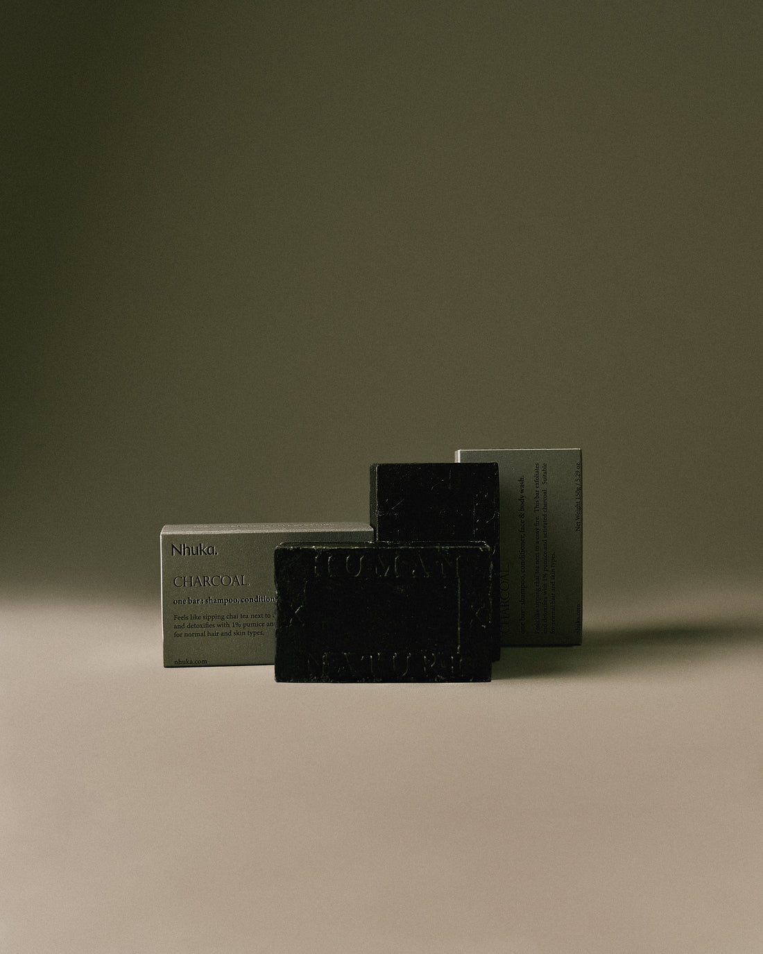 Nhuka Charcoal One Bar packaged in FSC-certified paper. Handmade in Australia, pH-balanced, sulfate-free, silicone-free, and organic. Warming chai scent with cinnamon, ginger, and nutmeg. Exfoliating formula with pumice, designed for hair, face, and body.