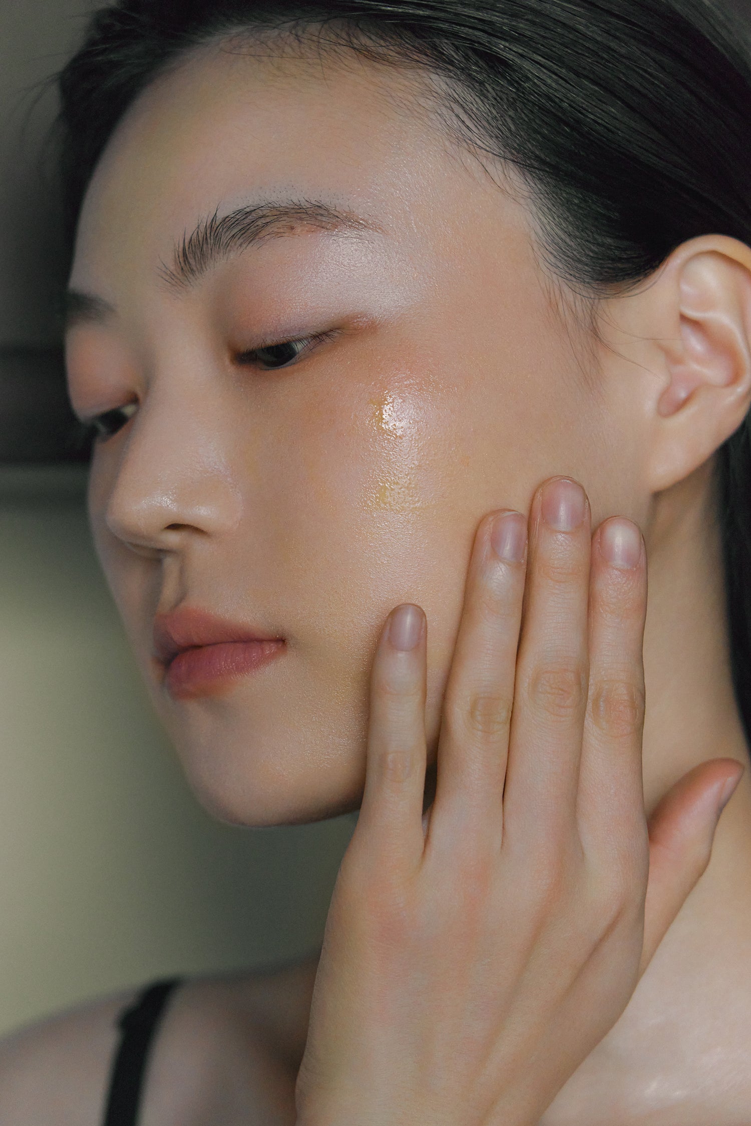 Model applying Nhuka Organic Face Serum to cheek.  Model applying Nhuka face serum to cheek. Skin glows with lightweight hydration from a blend of plant oils and actives, suitable for dry, mature, or sensitive skin types.