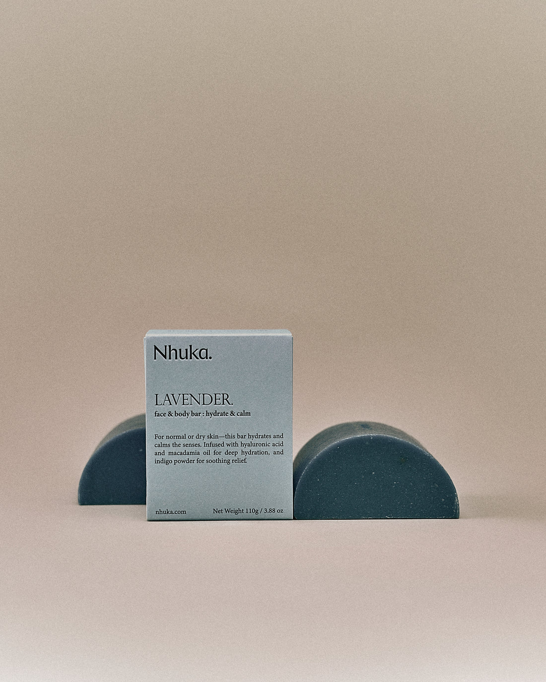 Nhuka organic lavender face and body soap with FSC-certified paper packaging, flanked by two unwrapped bars. Handmade in Australia for hydration and calm.