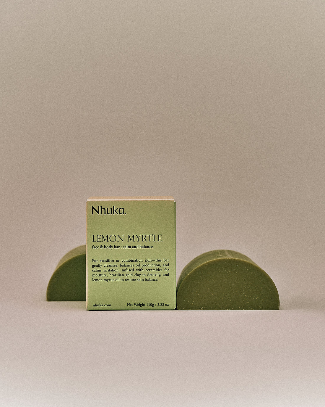 Nhuka organic lemon myrtle face and body soap with FSC-certified paper packaging, flanked by two unwrapped bars. Handmade in Australia for calming and balancing combination skin.