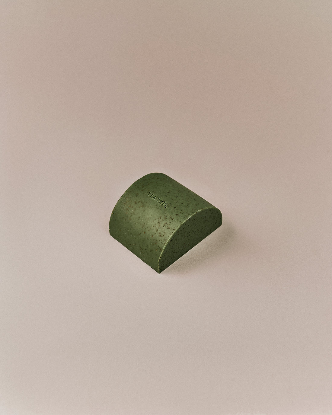 Nhuka organic tea tree soap bar shown at an angle. Solid exfoliating soap with green clay, tea tree leaf, and menthol for blemished skin.