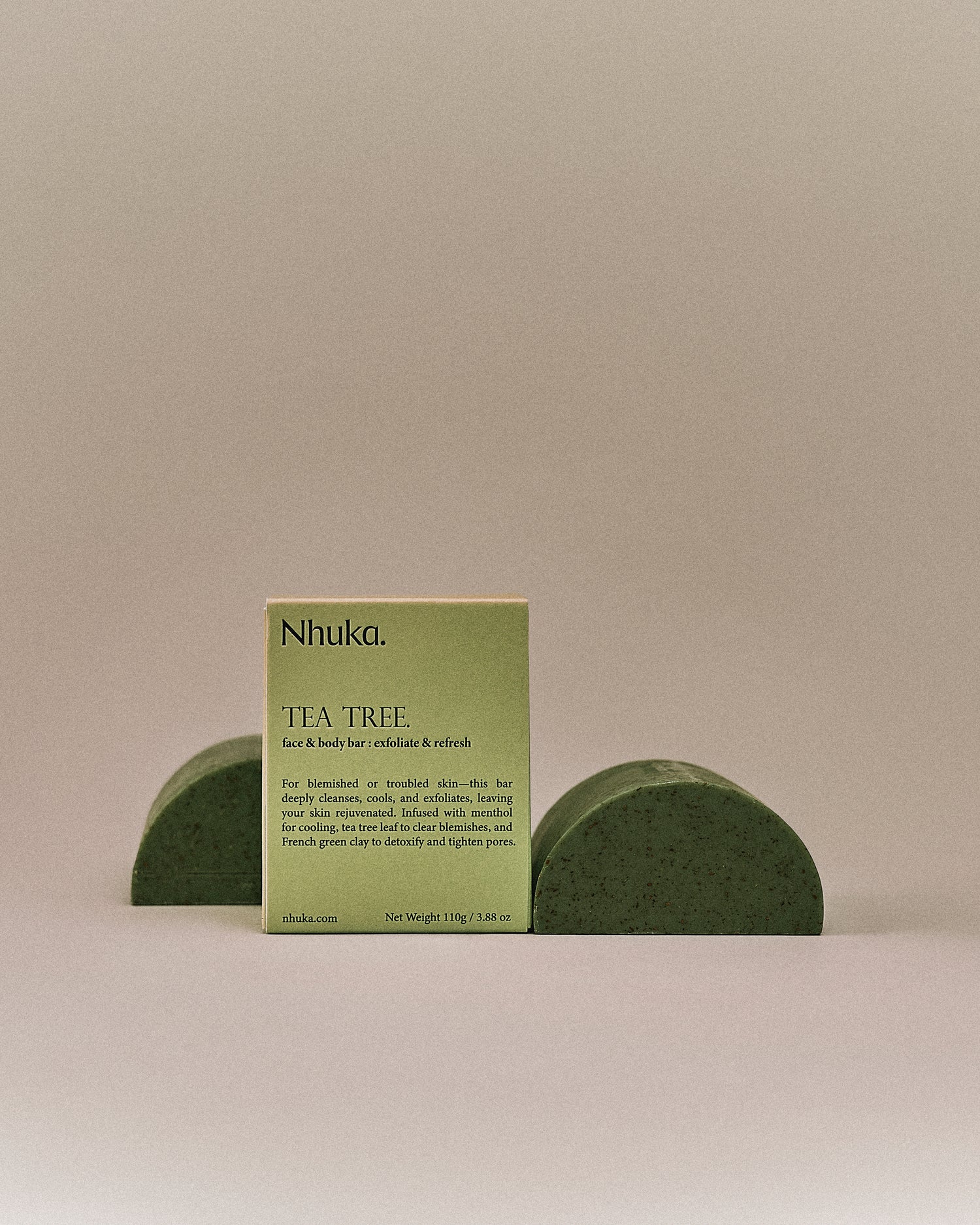 Nhuka organic tea tree face and body soap with FSC-certified paper packaging, flanked by two unwrapped bars. Handmade in Australia to exfoliate, cool, and refresh troubled skin.