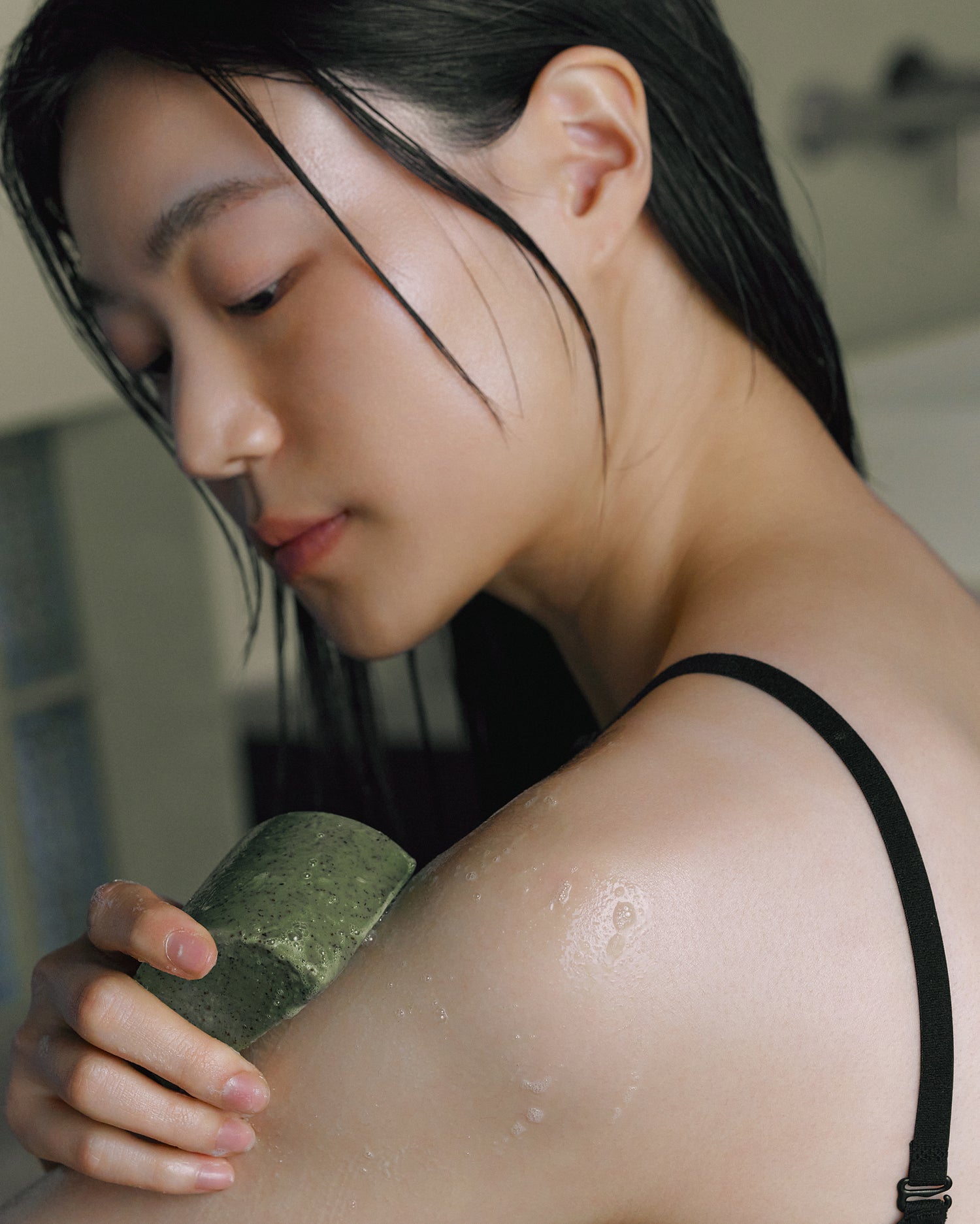 Model applying Nhuka organic tea tree soap to shoulder. Fresh green bar designed to cool, exfoliate, and refresh blemish-prone skin.