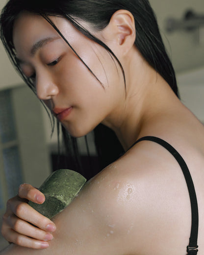 Model applying Nhuka organic tea tree soap to shoulder. Fresh green bar designed to cool, exfoliate, and refresh blemish-prone skin.