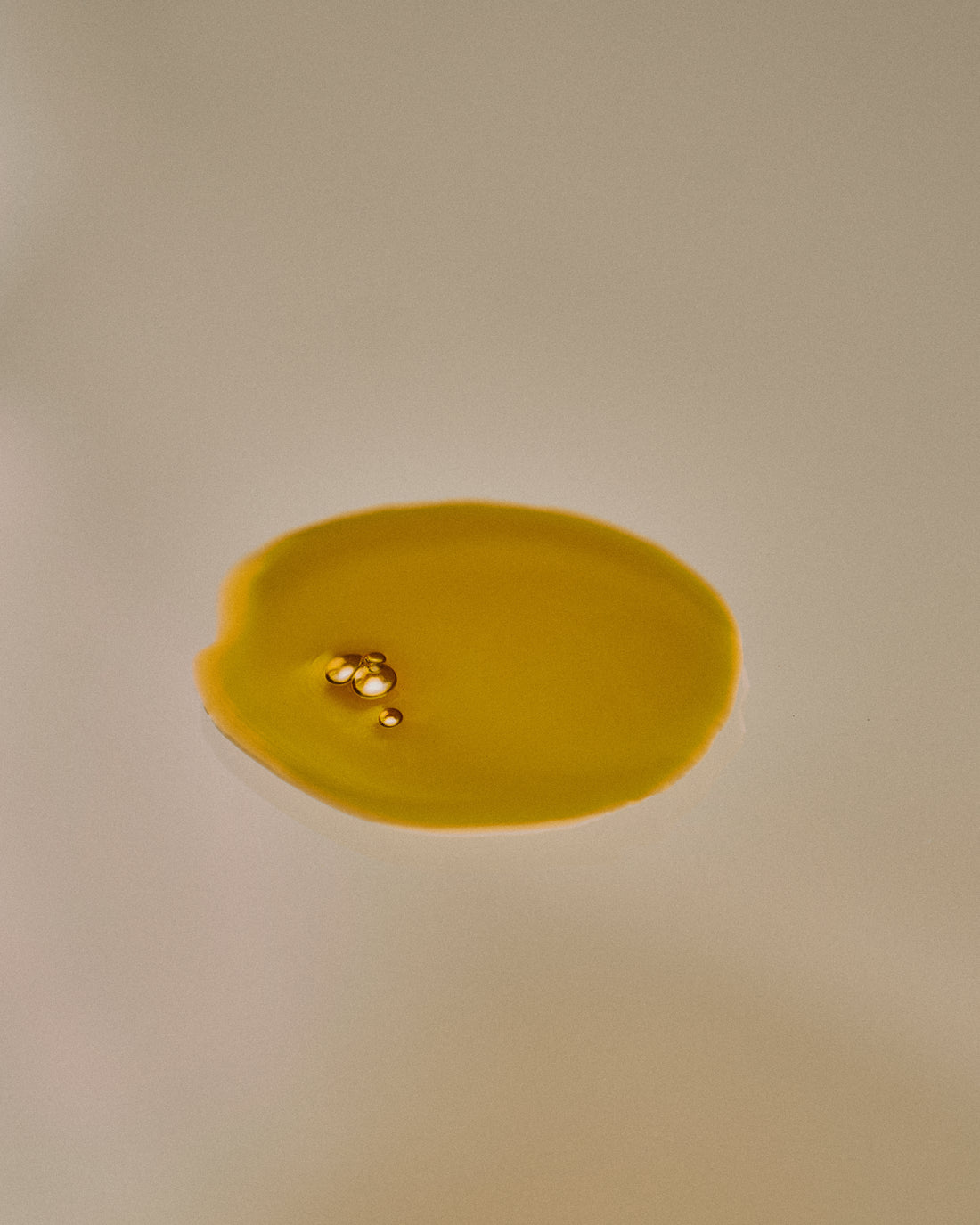 Nhuka Restoration Face Serum texture — golden oil droplets. Formulated with ceramides, hempseed, and rosehip oils to deliver calming hydration for sensitive skin.