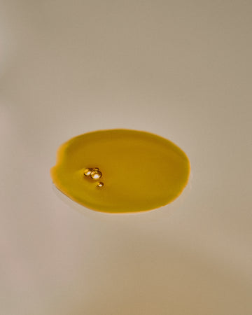 Nhuka Restoration Face Serum texture — golden oil droplets. Formulated with ceramides, hempseed, and rosehip oils to deliver calming hydration for sensitive skin.