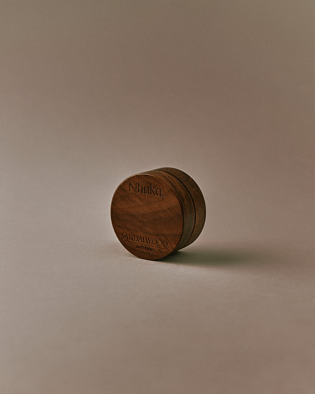 Nhuka Sandalwood Multi Balm shown at an angle. Rich yet silky balm formulated with organic shea butter, hempseed oil, and beeswax to nourish and soothe dry or sensitive skin. Features a warm, earthy scent with hints of sandalwood, sage, and vanilla.