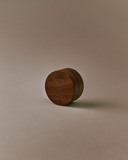 Nhuka Sandalwood Multi Balm shown at an angle. Rich yet silky balm formulated with organic shea butter, hempseed oil, and beeswax to nourish and soothe dry or sensitive skin. Features a warm, earthy scent with hints of sandalwood, sage, and vanilla.