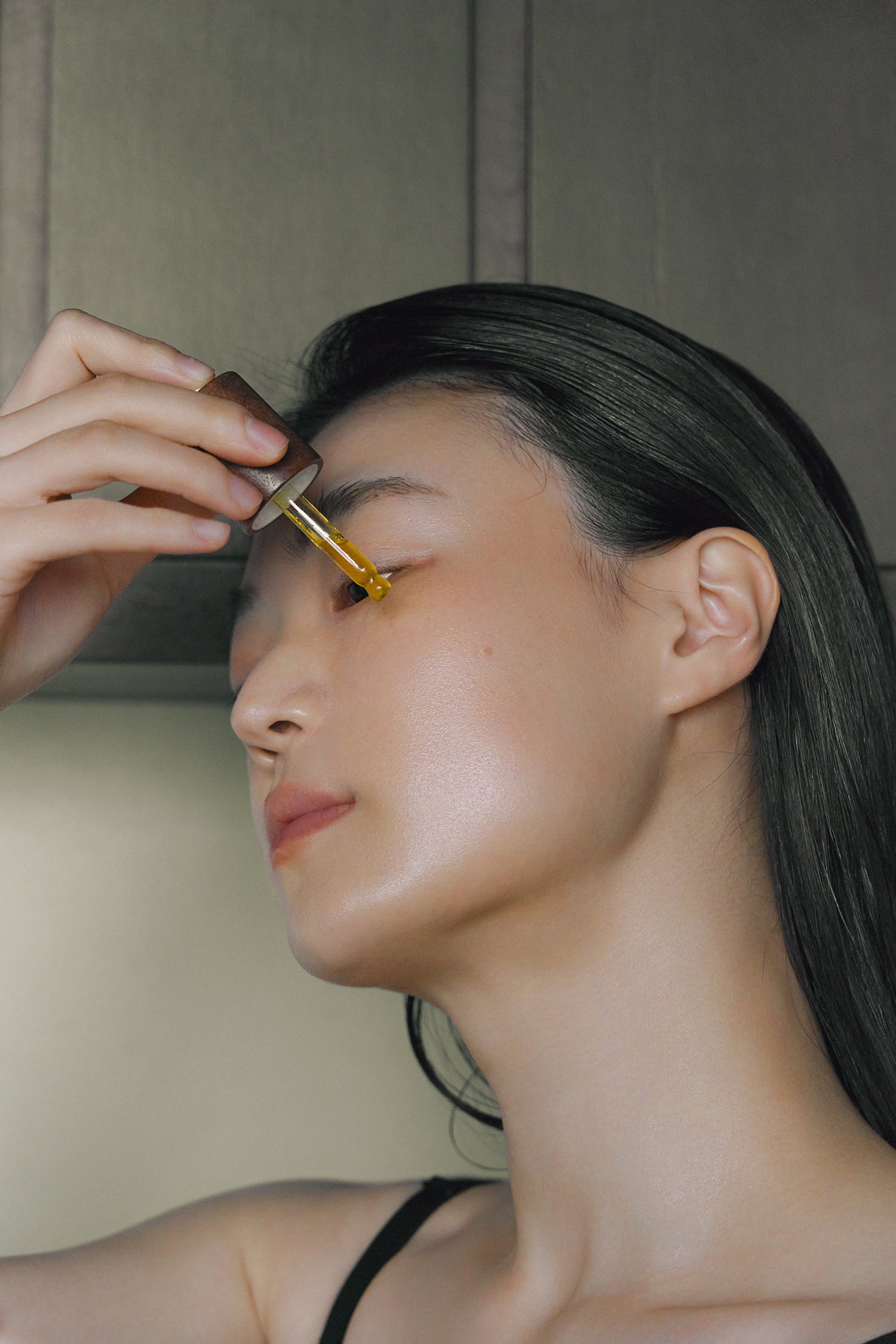 Model applying Nhuka Stillness Face Serum with dropper near the eye area. Brightening serum with 1% bakuchiol oil and 5% vitamin C for mature or dry skin.