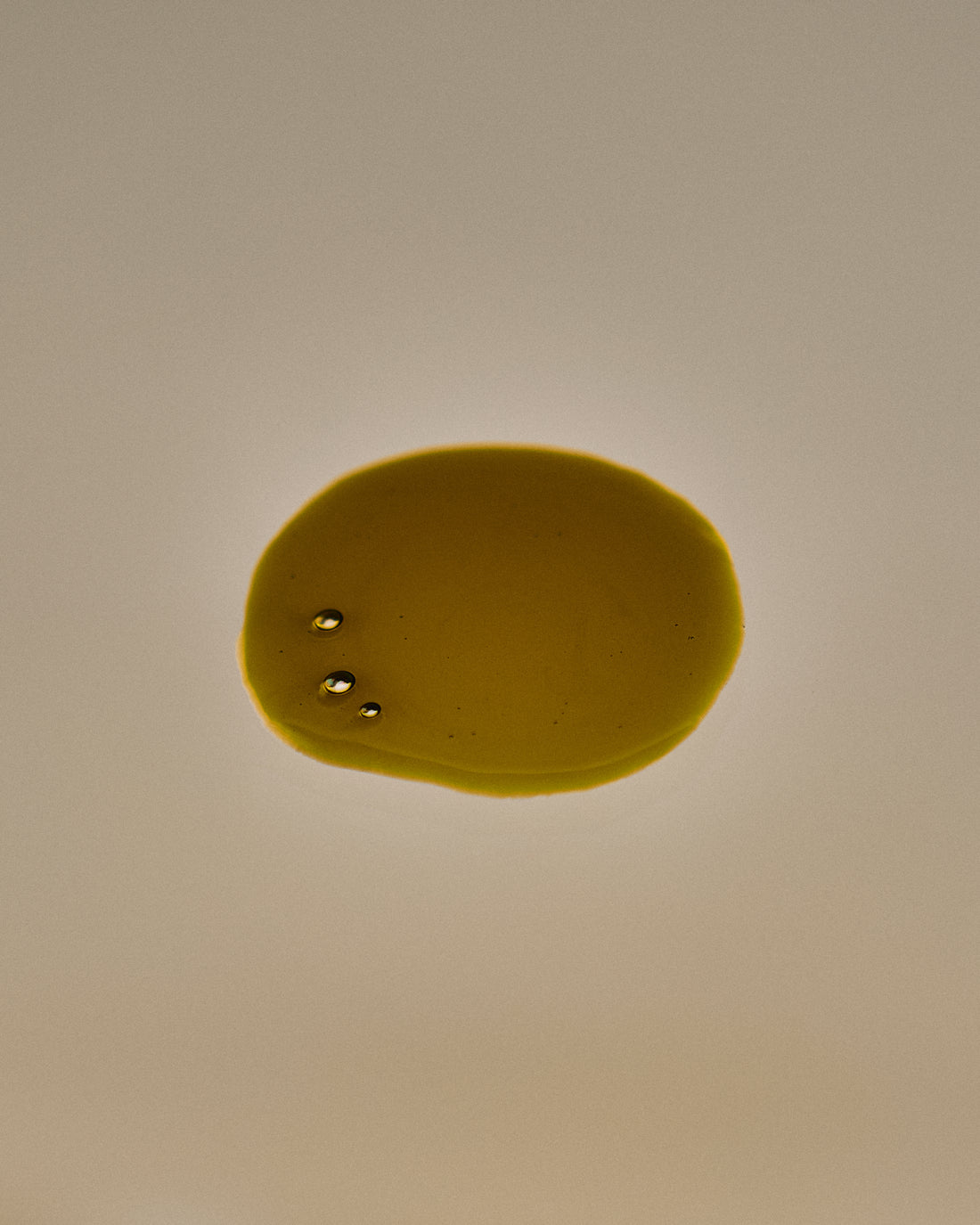 Nhuka Stillness Face Serum texture with green gold drops. Nourishing organic oil serum with 1% bakuchiol and 5% vitamin C for deep hydration and skin glow.