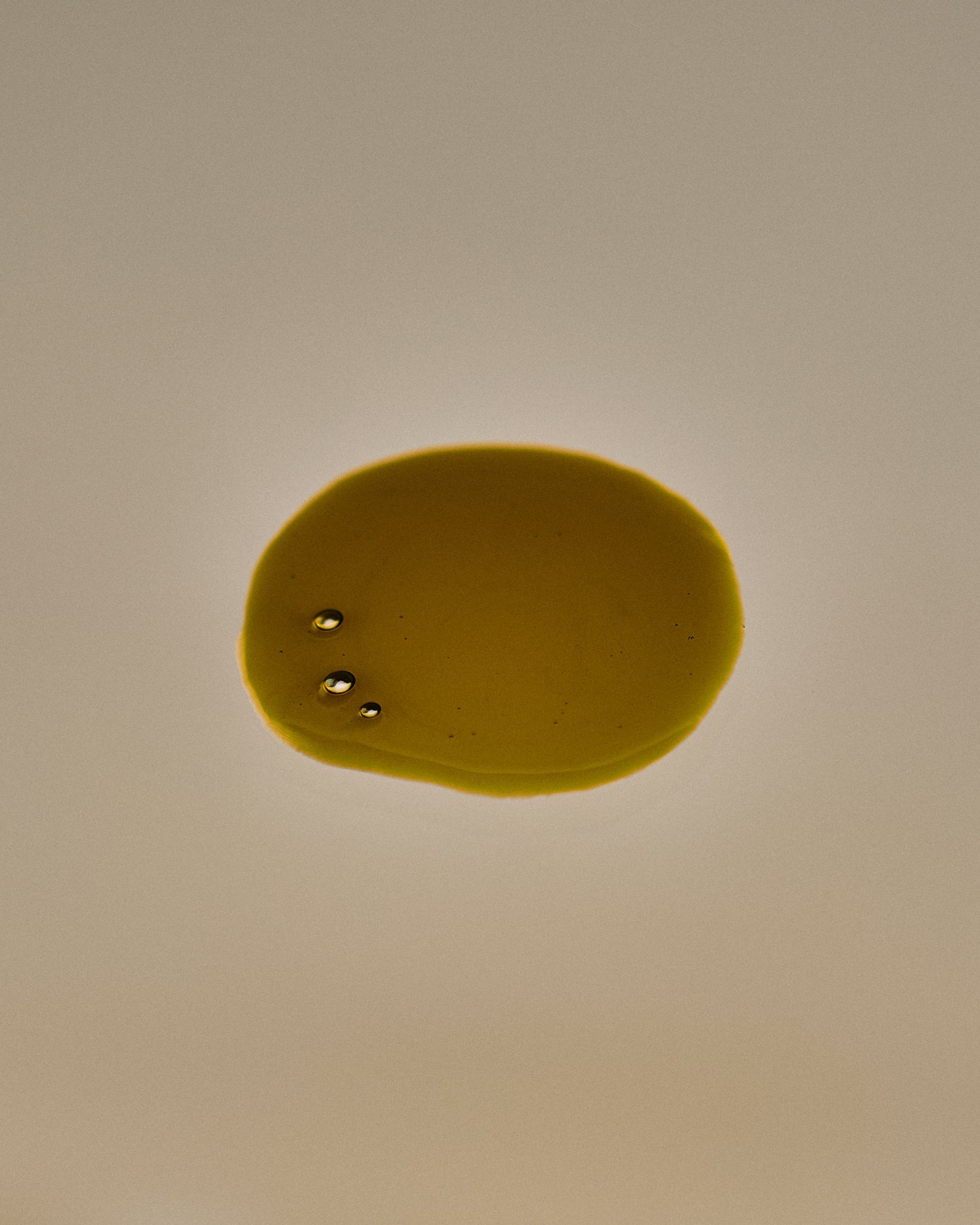 Nhuka Stillness Face Serum texture with green gold drops. Nourishing organic oil serum with 1% bakuchiol and 5% vitamin C for deep hydration and skin glow.